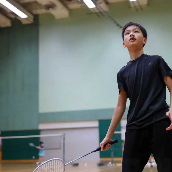 Dreng med badmintonketsjer følger fjerbolden i en idrætshal